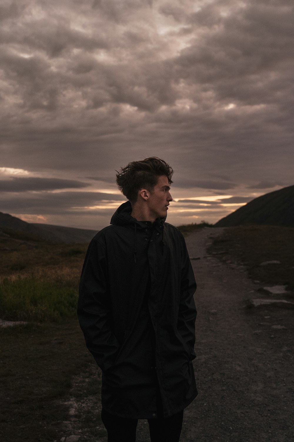 a man standing on a dirt road under a cloudy sky