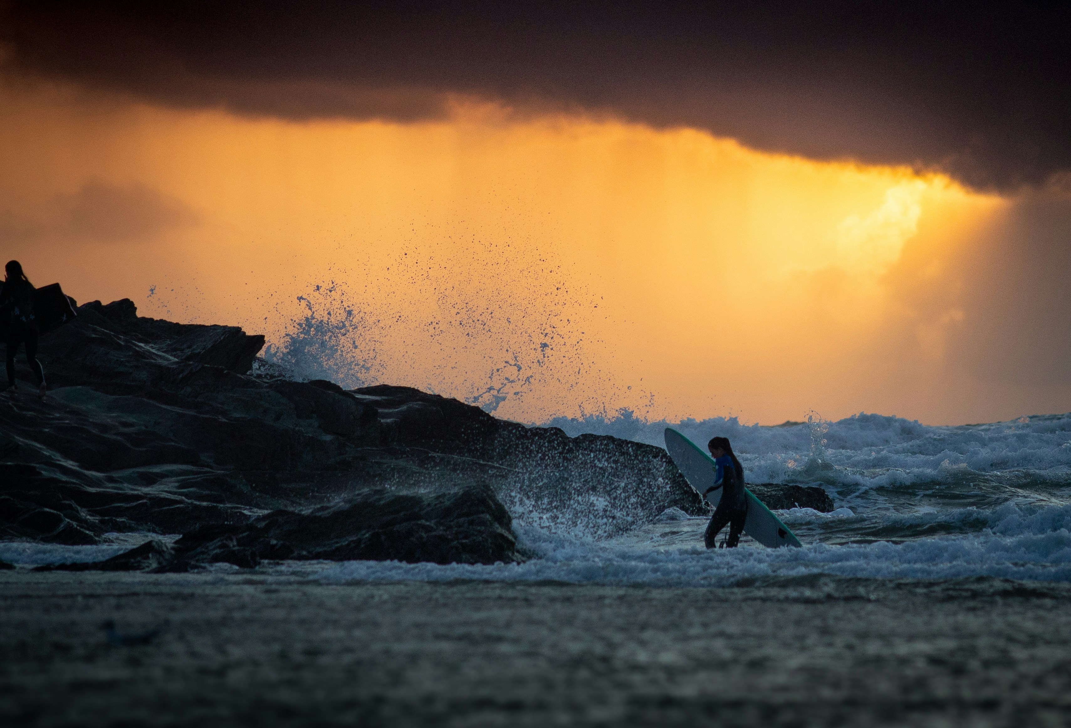 woman carrying surfboard standing on shore during golden hour