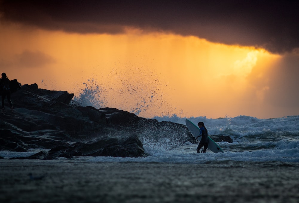 woman carrying surfboard standing on shore during golden hour