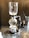A coffee siphon apparatus is set up on a countertop. It features a glass chamber on top, connected to a spherical bottom chamber. A visible flame is underneath, heating the lower chamber. The setup is sophisticated and suggests precision in brewing coffee.