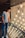 A person is standing on a staircase with a glass railing, looking at a display of numerous hanging light bulbs. These bulbs are arranged in rows with visible filaments and create a warm, glowing ambiance. The person is wearing a graphic t-shirt with text and jeans, and they are gazing intently at the lights.