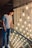 A person is standing on a staircase with a glass railing, looking at a display of numerous hanging light bulbs. These bulbs are arranged in rows with visible filaments and create a warm, glowing ambiance. The person is wearing a graphic t-shirt with text and jeans, and they are gazing intently at the lights.