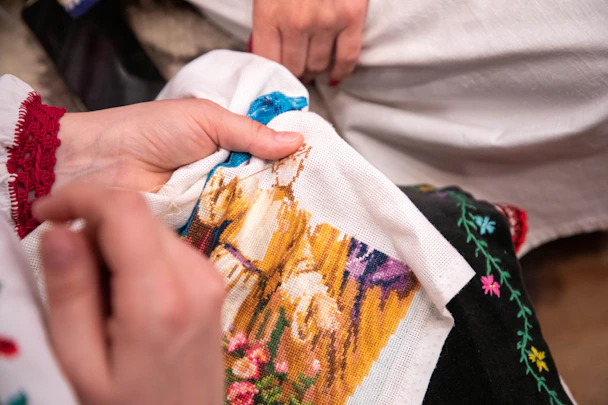 Close-up of artisan hands delicately stitching a vibrant floral pattern on a wedding hoop.