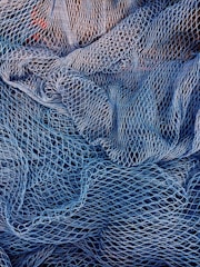 A complex mesh of intertwined fishing nets in varying shades of blue and white. The nets are intricately layered, creating a textured pattern with gaps and openings of different sizes.
