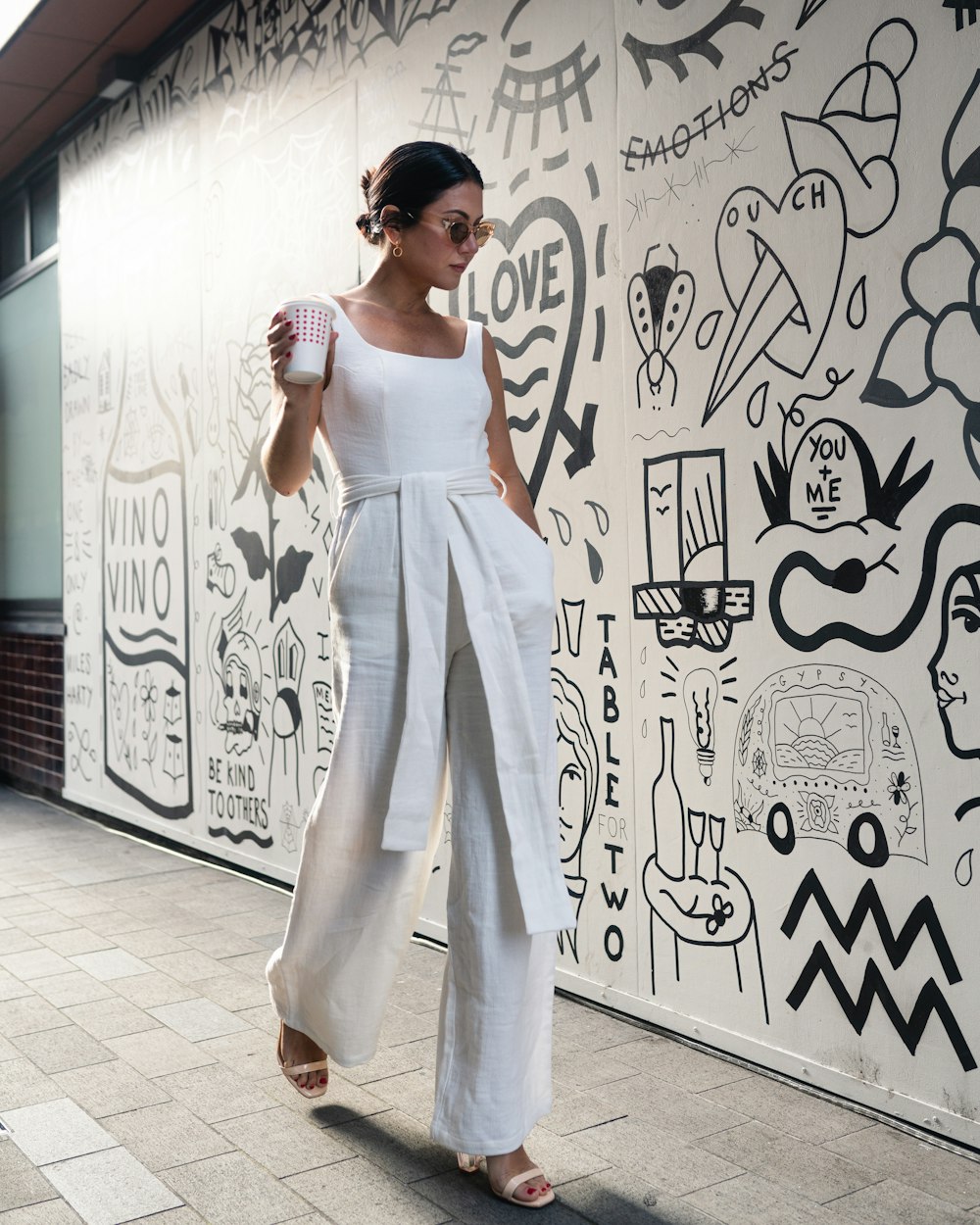 woman holding cup walking beside wall