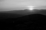 Black and white photograph capturing a serene mountain landscape at dawn.