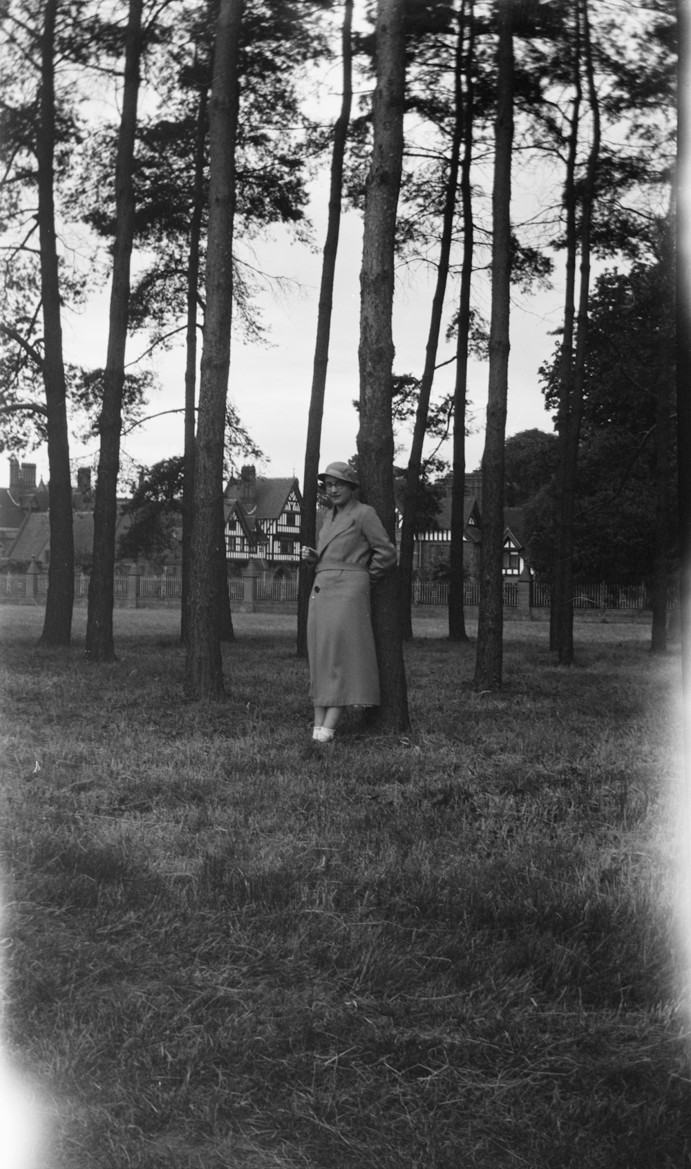 grayscale photography of woman standing and leaning on tree