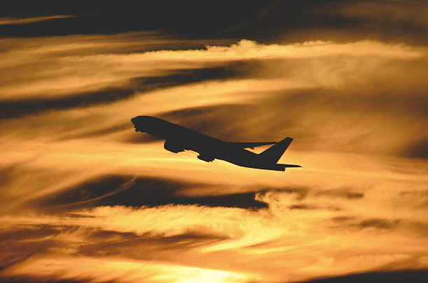 A sleek airplane soaring above clouds under a deep blue sky with a golden sunrise.