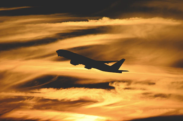 Sunset silhouette of an airplane soaring above the clouds.