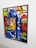 A vibrant, abstract painting featuring a mosaic pattern. A central prominent element is a single eye, partially visible behind colorful geometric shapes. The artwork combines a diverse mix of colors and symbols, including stars and swirl motifs.