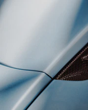 A vibrant close-up of an auto body painting process showing smooth, glossy navy blue paint being applied with a professional spray gun.