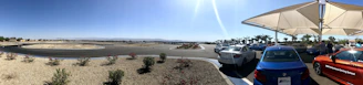 A wide view of the race track parking area filled with cars on race day under a clear sky.
