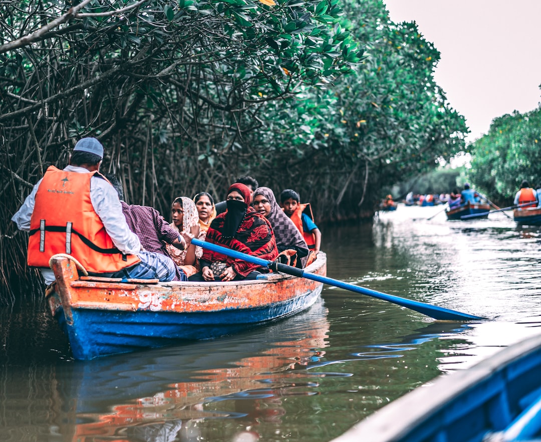 people riding blue and orange boat besides green plants