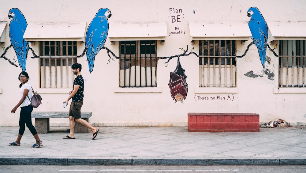 two people walking near white painted wall during daytime