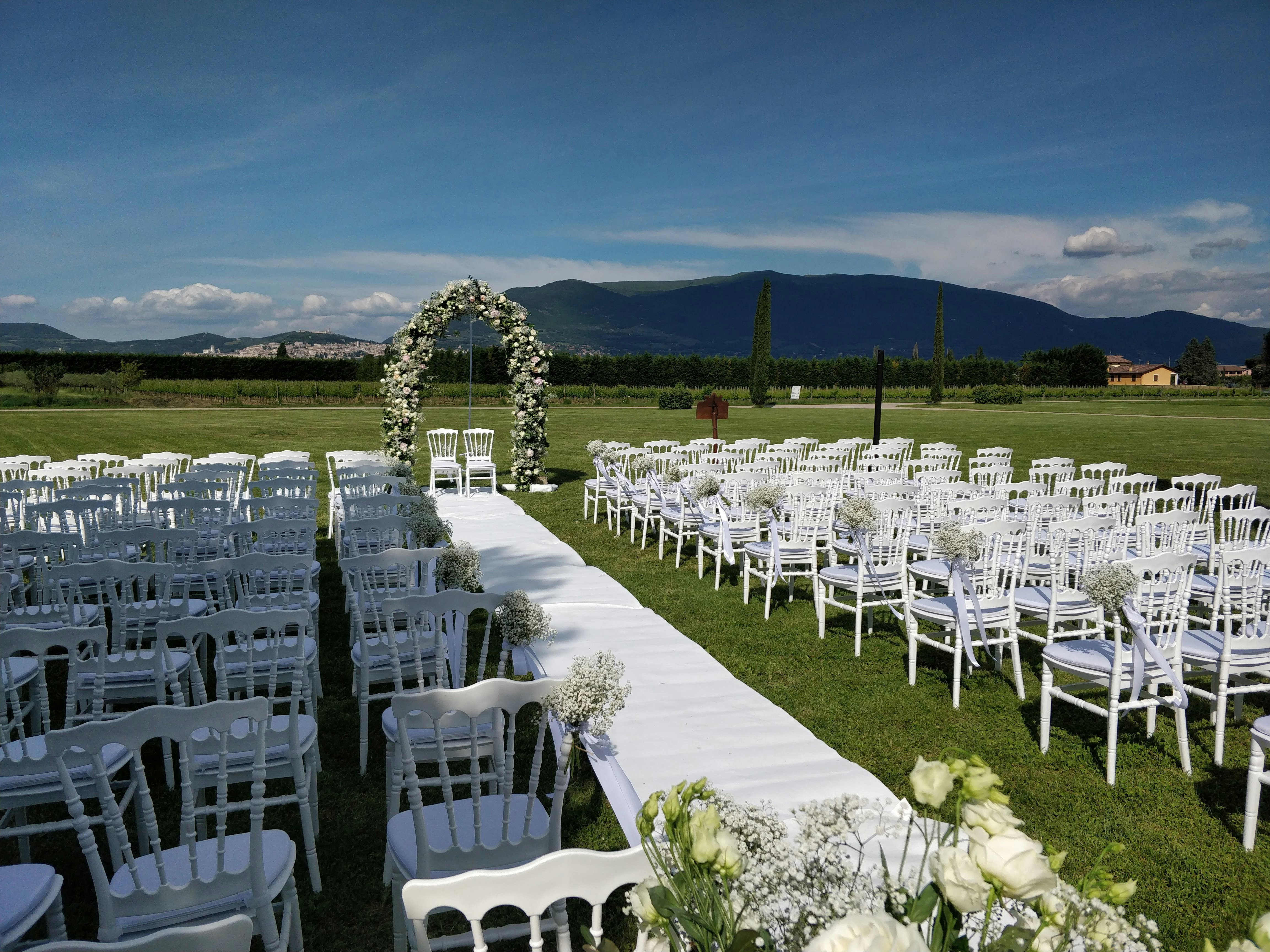 Elegant wedding ceremony setup with white chairs arranged in rows leading to floral arch with soft natural lighting