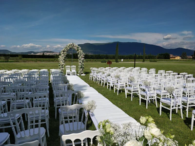 Guests seated on wooden chairs facing the floral arch under a clear blue sky.