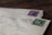 Two vintage envelopes are stacked on a wooden surface, each with distinctive postmarks and colorful stamps. The top envelope features a green stamp with the word 'SUOMI' and 'FINLAND,' while the envelope below has a purple stamp.