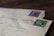 Two vintage envelopes are stacked on a wooden surface, each with distinctive postmarks and colorful stamps. The top envelope features a green stamp with the word 'SUOMI' and 'FINLAND,' while the envelope below has a purple stamp.