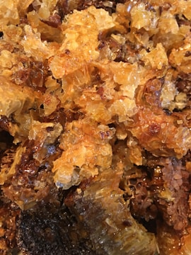 A close-up view of natural honeycomb, with a mix of golden and amber hues, showing intricate textures and details of the wax structure and honey.