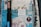 A textured urban wall with layers of torn posters and graffiti, featuring a prominent black pole with colorful stickers, a white paper with text, and a sticker advertising street art tours. The wall displays varied patterns and remnants of old advertisements, creating an eclectic and somewhat chaotic visual.