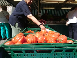 Close-up of a shopper's hand selecting ripe tomatoes from a wooden crate.