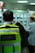A person wearing a high-visibility security vest stands in a retail environment. The background is slightly blurred, showing other people and shelves stocked with products.