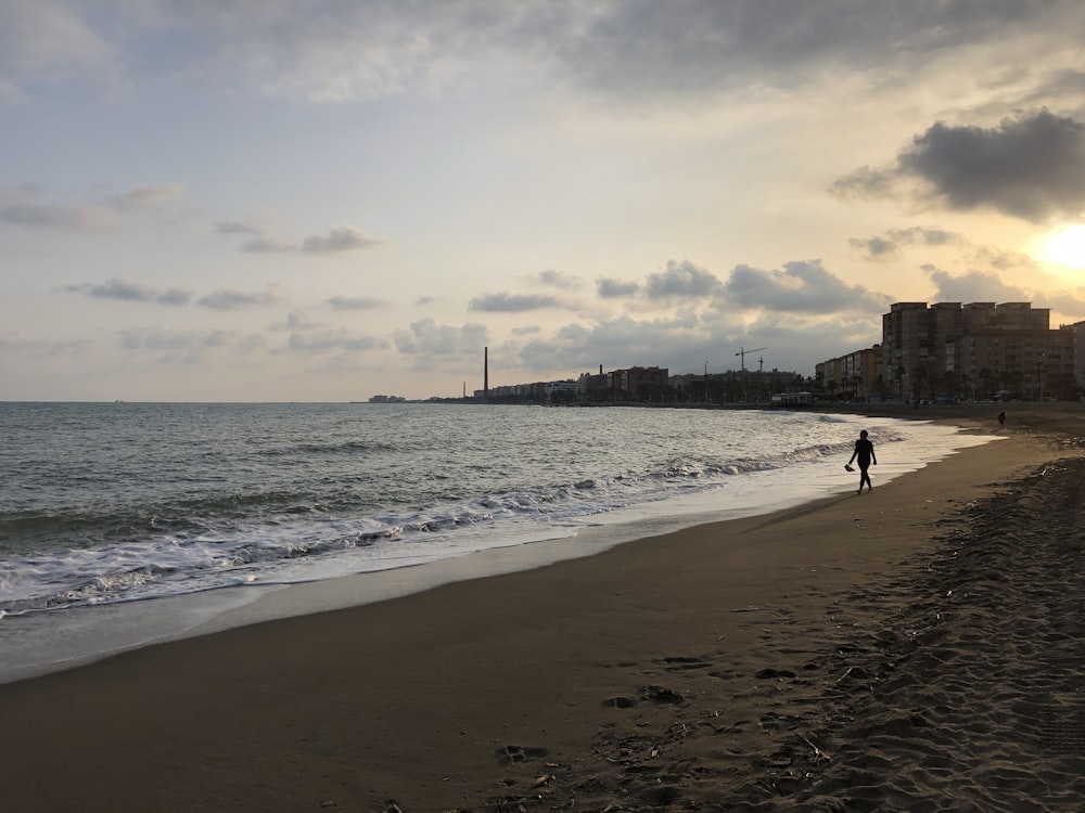 man walking on seashore near sea during daytime