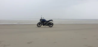 A solitary enduro bike parked on a sandy ridge overlooking a vast desert landscape under a moody sky.