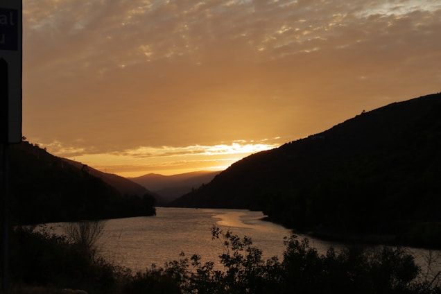 A serene landscape photo capturing golden hour light over rolling hills and a calm river.