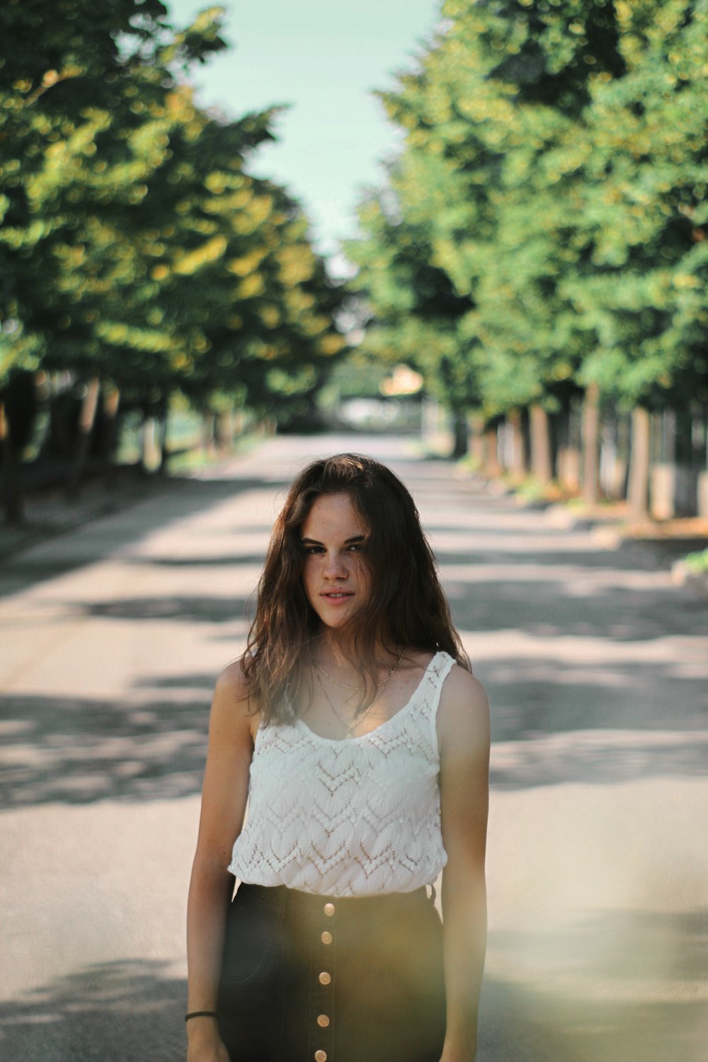 girl standing on road between trees
