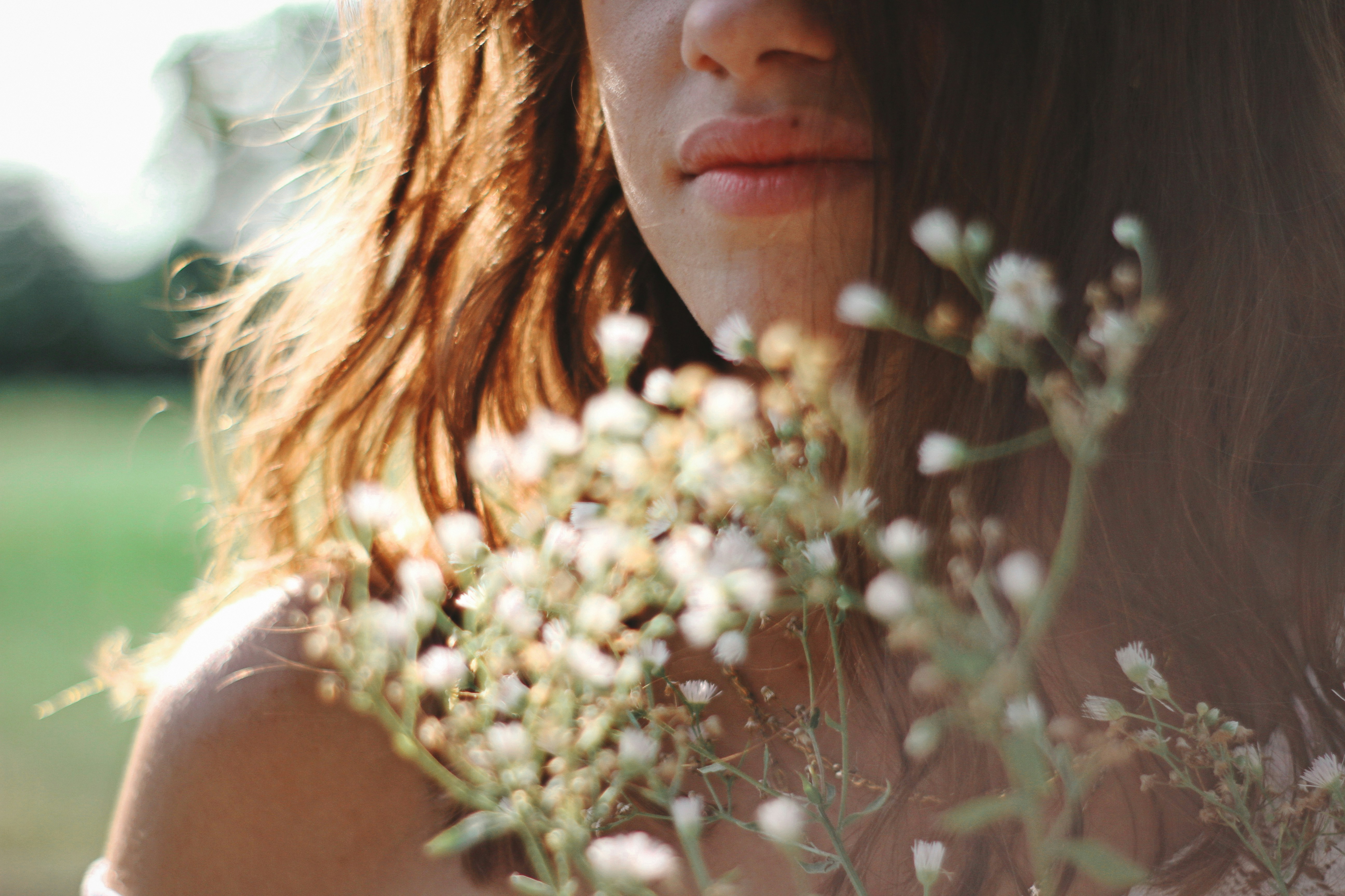 A woman with long hair holds a bouquet of colorful flowers, smiling gently in a natural outdoor setting.