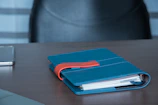 Bright orange notebook with pens and a phone showing study app.
