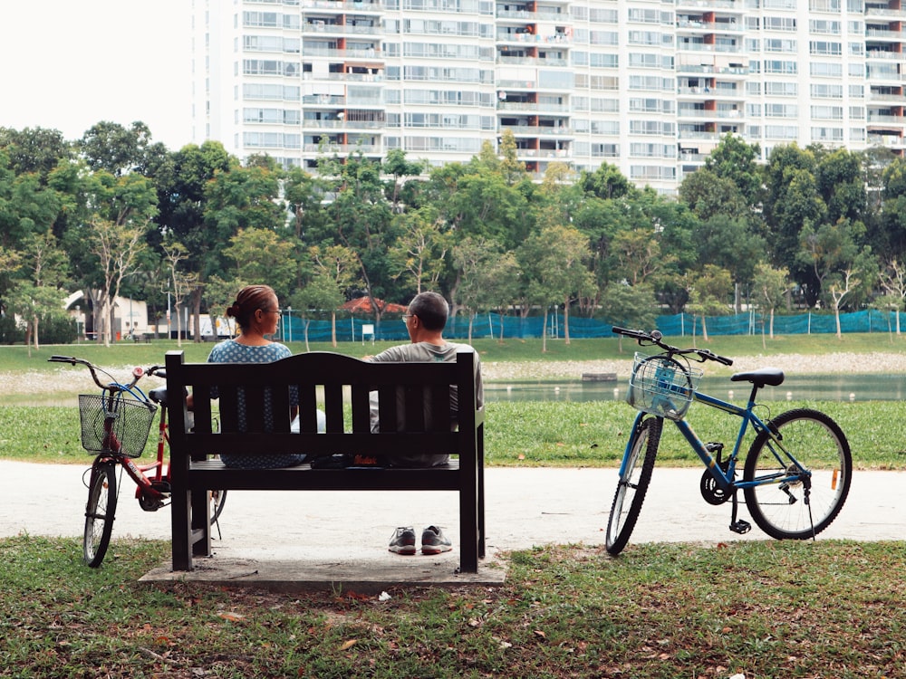 昼間、2台の自転車のそばのベンチに座って緑の野原を眺める男女
