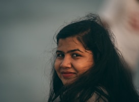 A woman with long dark hair and a gentle smile gazes towards the camera. The background is softly blurred, creating a serene and intimate atmosphere.