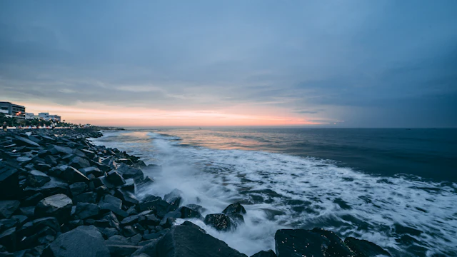 Waves on dark rocks under an orange and blue dawn sky, Pondicherry