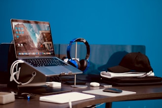 turned-on laptop beside headphones and cap on desk