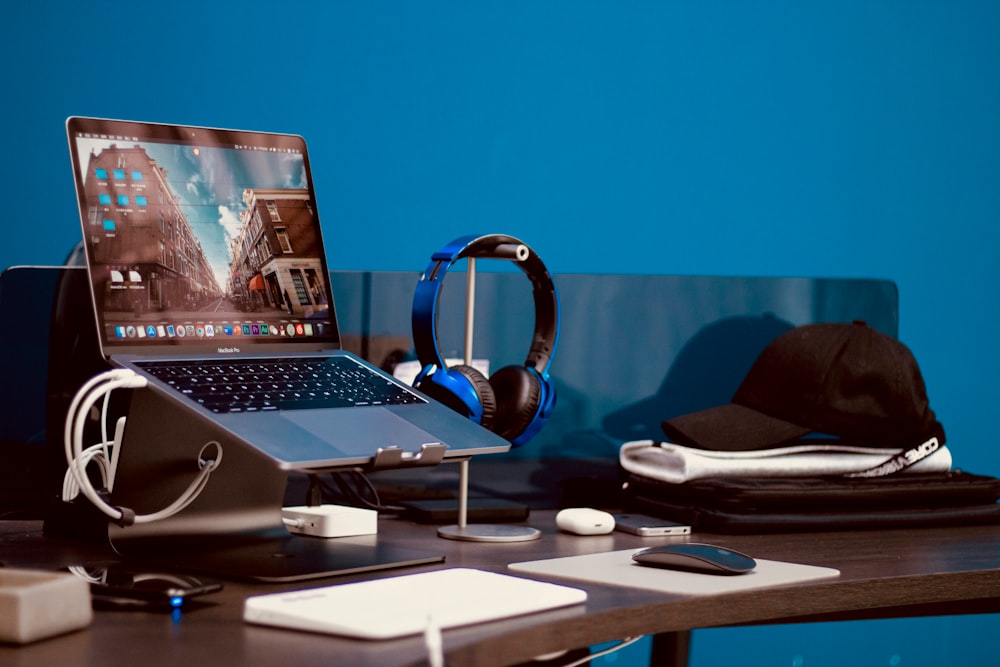 turned-on laptop beside headphones and cap on desk