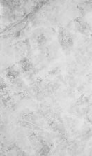 A textured surface with a marbled pattern predominantly in light grey tones. The design features various shades of grey, interspersed with subtle vein-like lines and patches that contribute to a natural stone appearance.