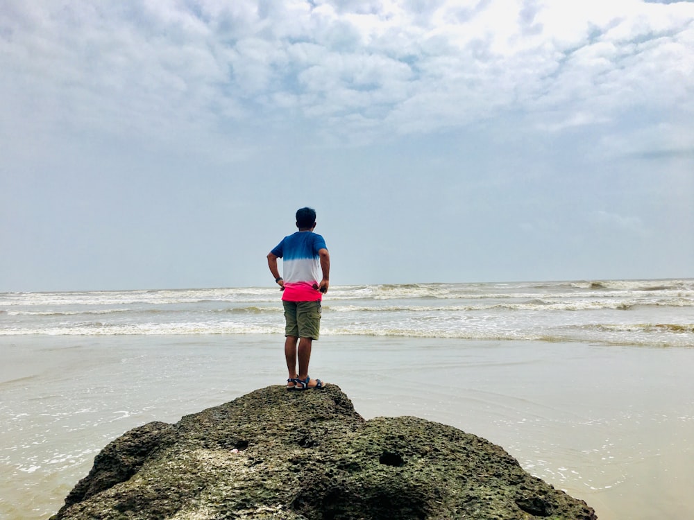 person in blue, white, and pink T-shirt standing in front of ocean during daytime