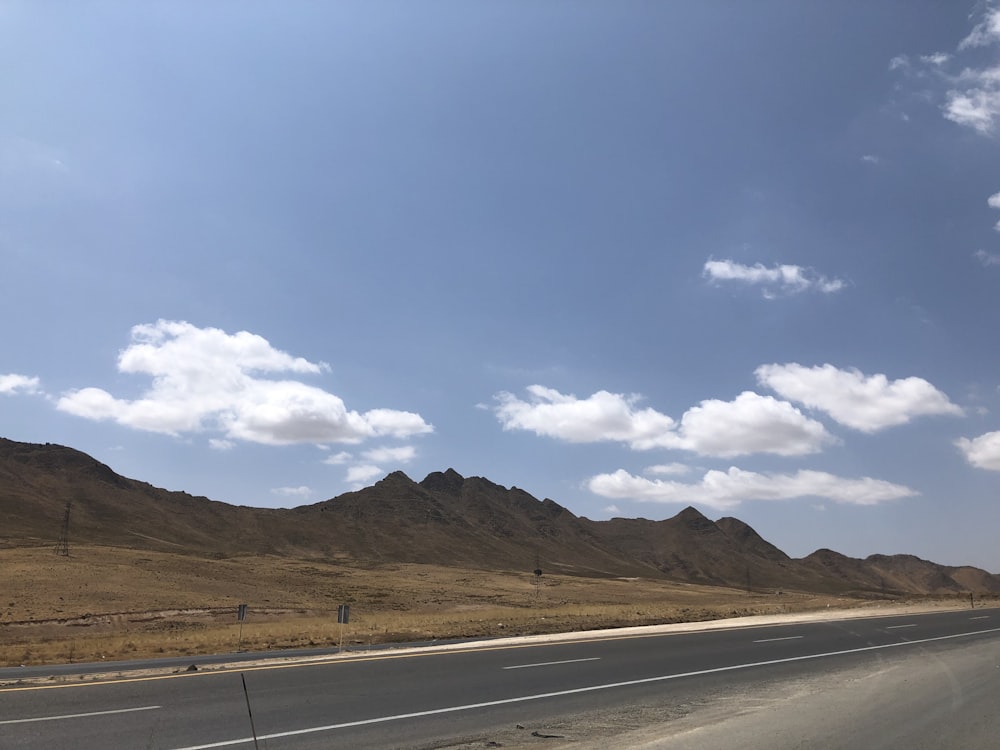 gray concrete road viewing mountain under blue and white sky during daytime