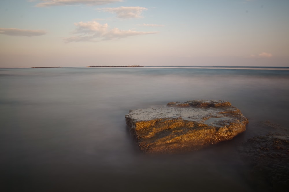 brown rock in body of water under blue and white sky