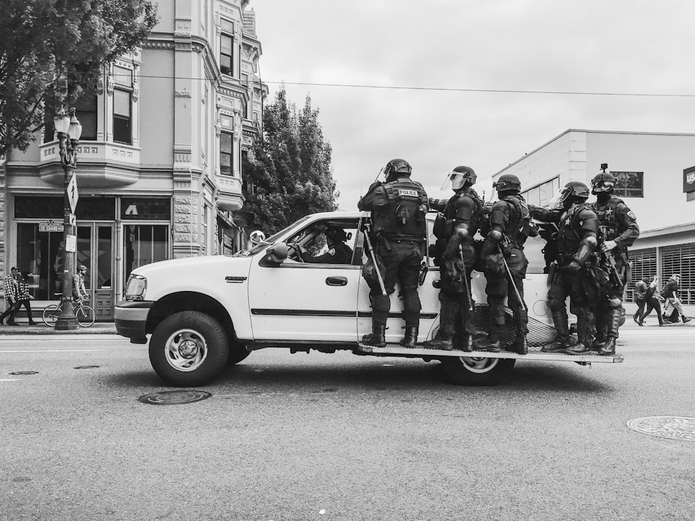 grayscale photo of men standing beside vehicle