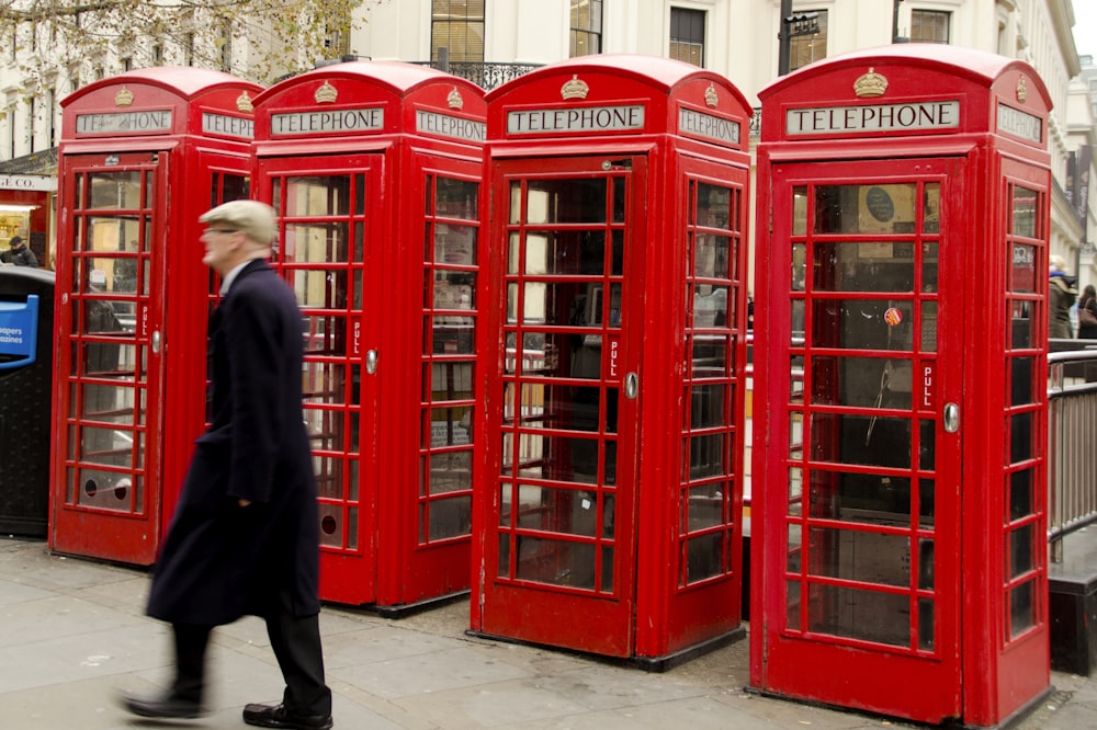 man walking near red telephone booth during daytime