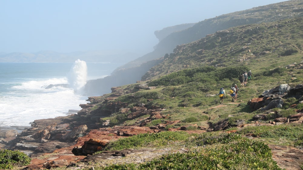 a group of people walking up a hill next to the ocean