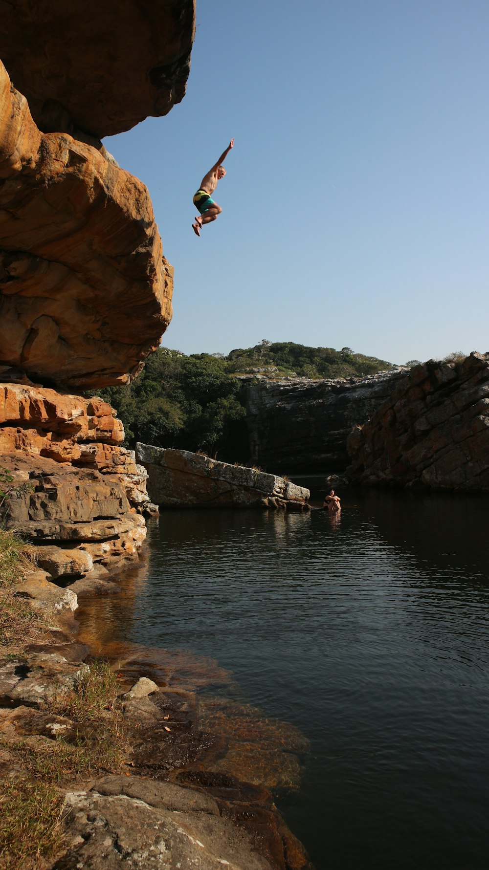 man jumping off rocky mountain above body of water