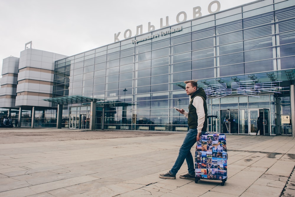 man sitting on rolling travel bag in front of building