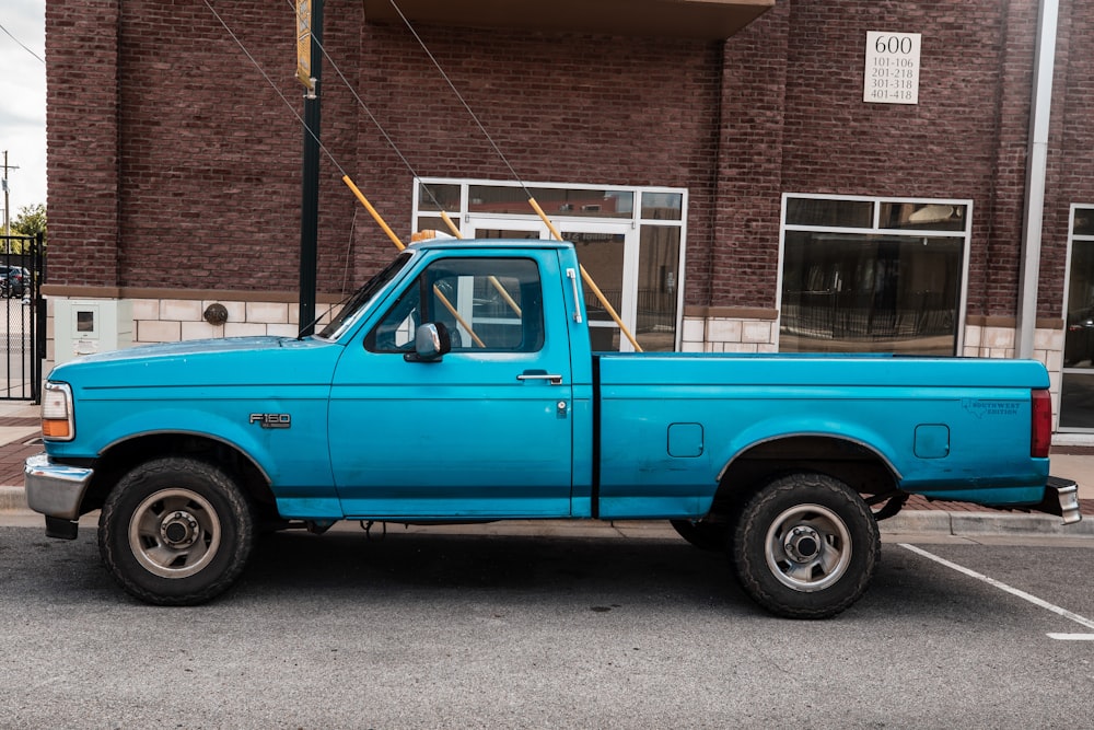 blue Ford F-150 regular cab pickup truck parked beside the road in front of brick building