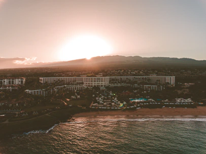 Cinematic drone shot of a luxury resort nestled between mountains and ocean at sunset.