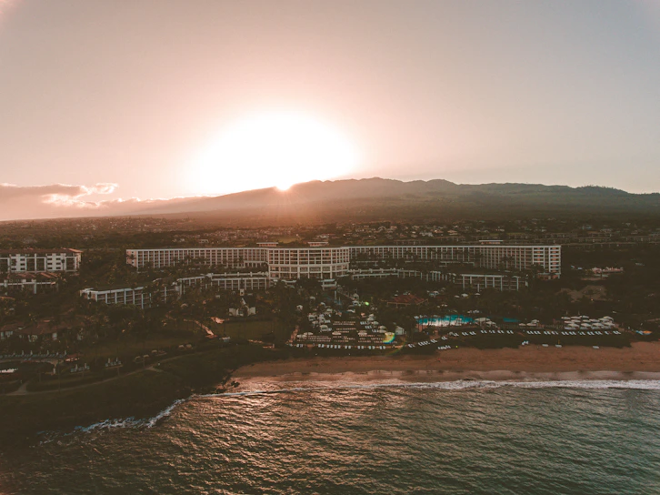 A sweeping aerial shot of a coastal resort at sunset, golden light reflecting off the water.
