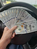 Cash being handed over to a smiling customer beside a removed old sedan.